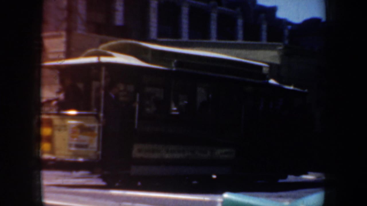 Dark trolley car passing older city buildings on a sunlit street.