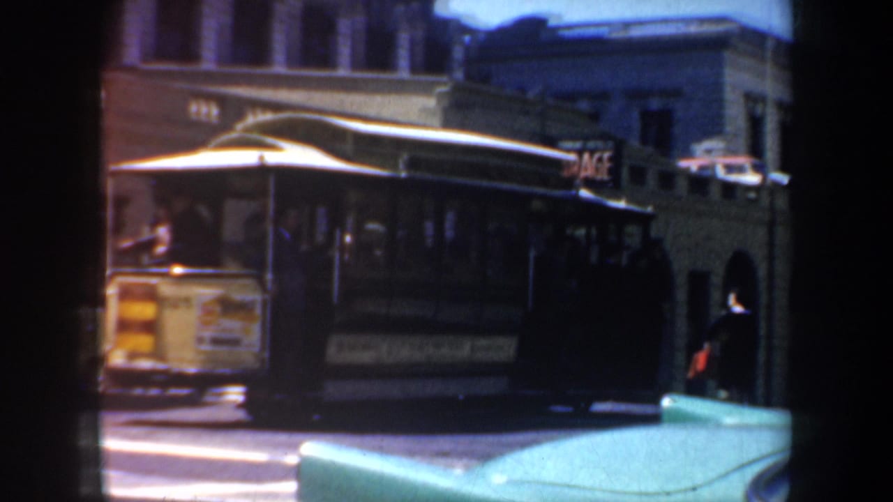 1957 San Francisco street view showing a trolley car, older buildings, and a partial GARAGE sign in a grainy 8mm frame.