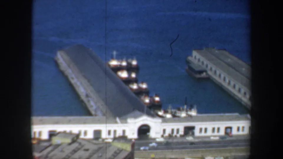 1957 San Francisco waterfront seen from above, showing long piers, docked small boats, bay water, pier buildings, and a road at the bottom edge.