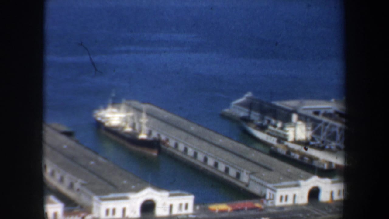 San Francisco waterfront footage from 1957 showing dock buildings, a ship at the pier, and bay water beyond.
