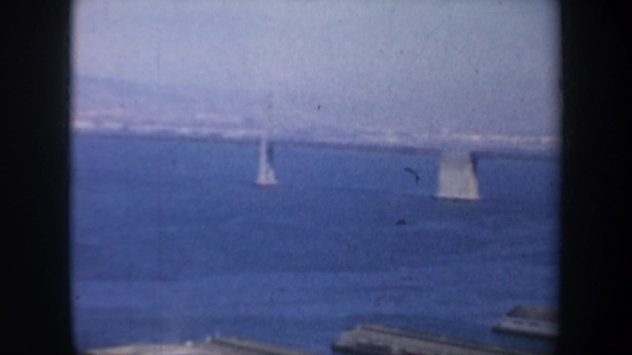 1957 San Francisco bay scene showing sailboats under a distant bridge, partially obscured by a central window mullion.