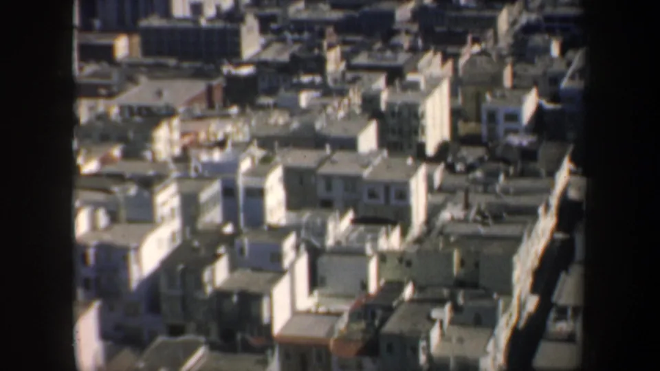 High-angle 1957 San Francisco city view with dense rooftops, streets, and downtown buildings seen past a dark window frame.