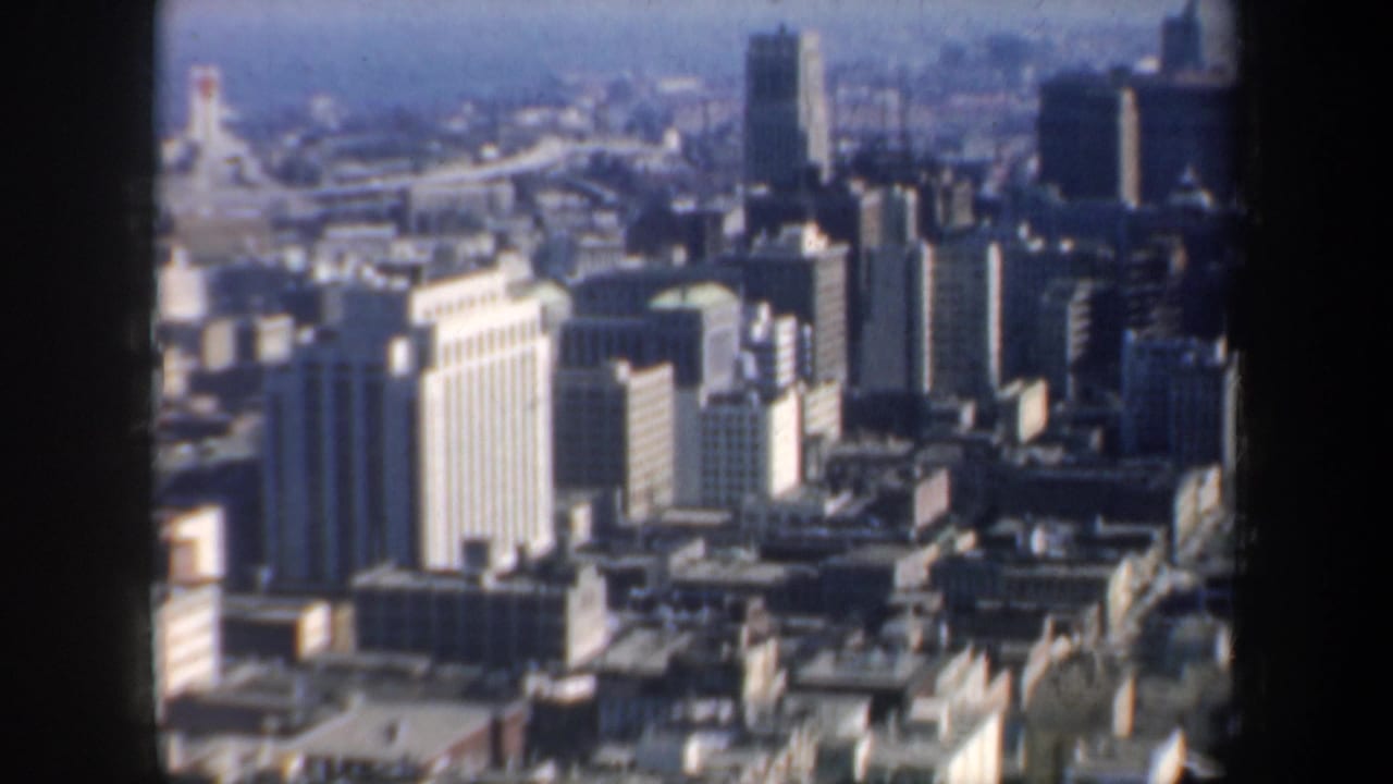 1957 San Francisco city skyline and dense rooftops viewed from above through a dark window frame on 8mm film.