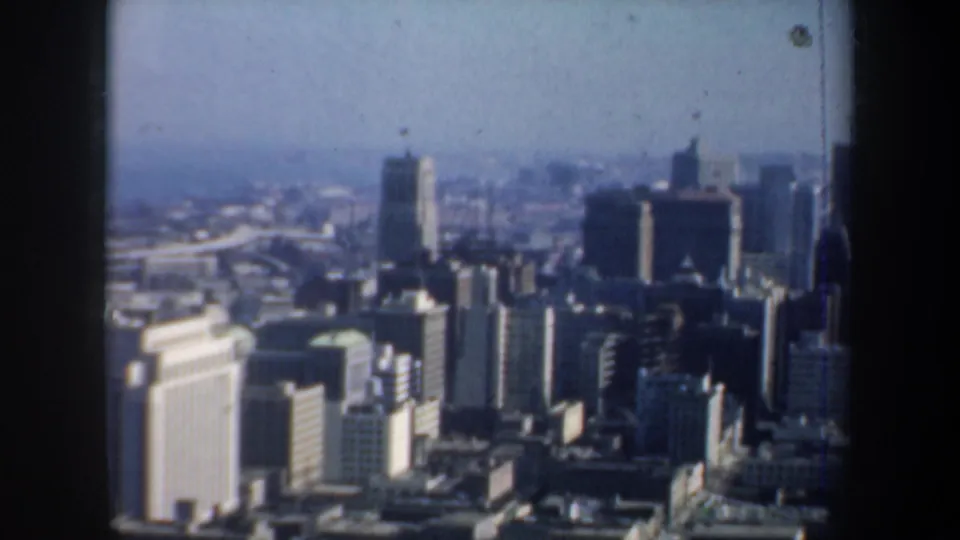 Aerial-style 1957 San Francisco view showing downtown buildings, rooftops, and haze through a window opening.