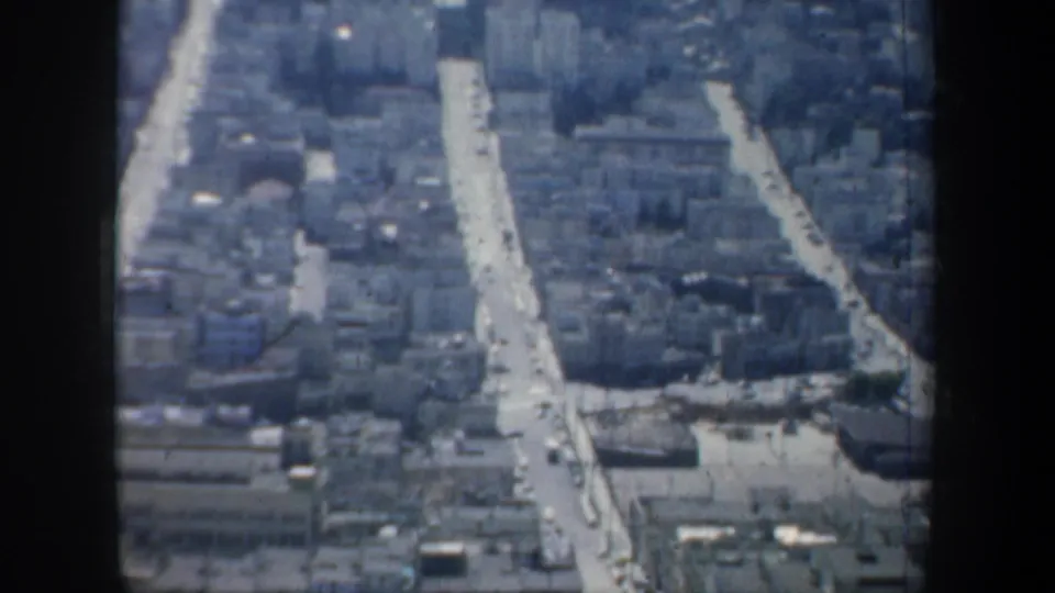 High-angle 1957 San Francisco street and rooftop view through glass, showing traffic traces and dense blocks.