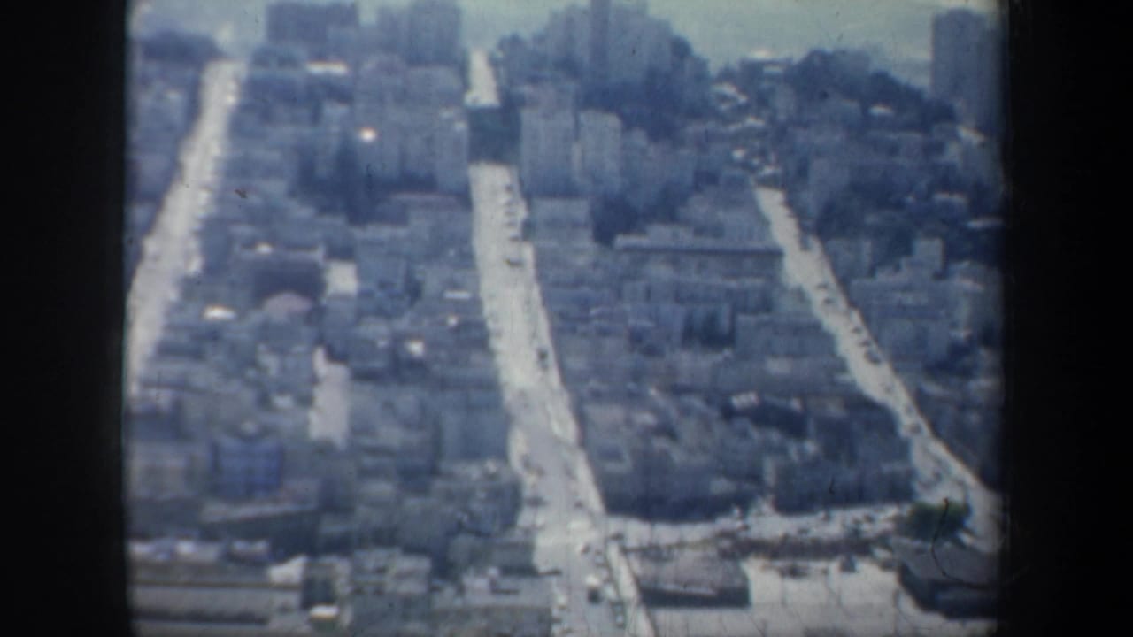 Elevated view over dense San Francisco streets and buildings with hazy hills beyond.