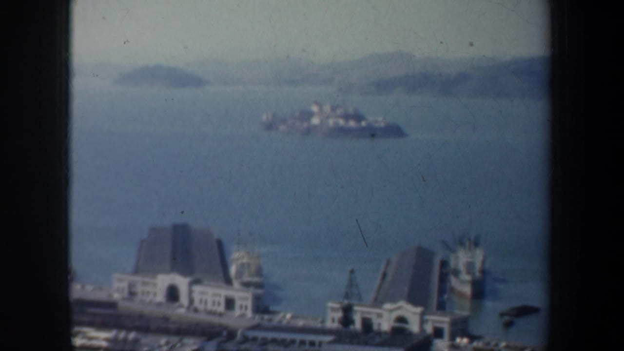 1957 San Francisco Bay view with Alcatraz Island in the distance and waterfront buildings below the window frame.