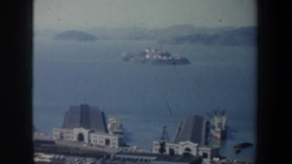 1957 San Francisco Bay view with Alcatraz Island in the distance and waterfront buildings below the window frame.