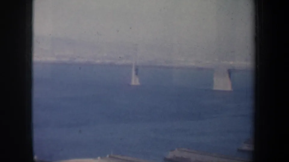Mid-century San Francisco Bay footage shows sailboats below a distant bridge, with soft exposure and dark foreground framing.