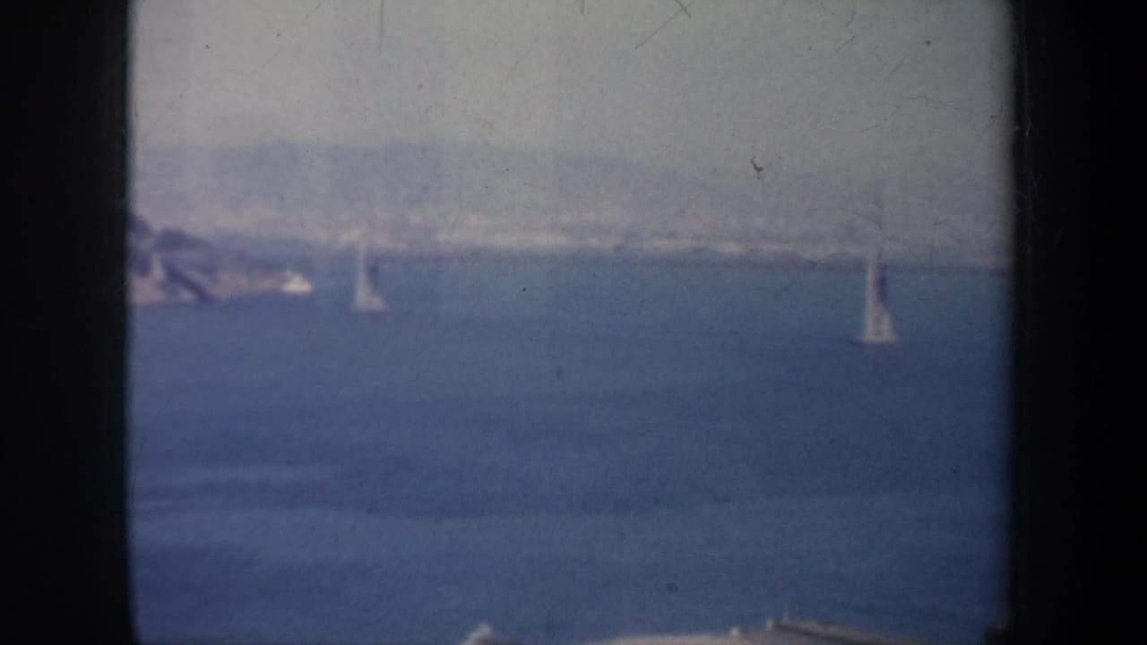 Bay water with small sailboats seen through dark film-frame edges.