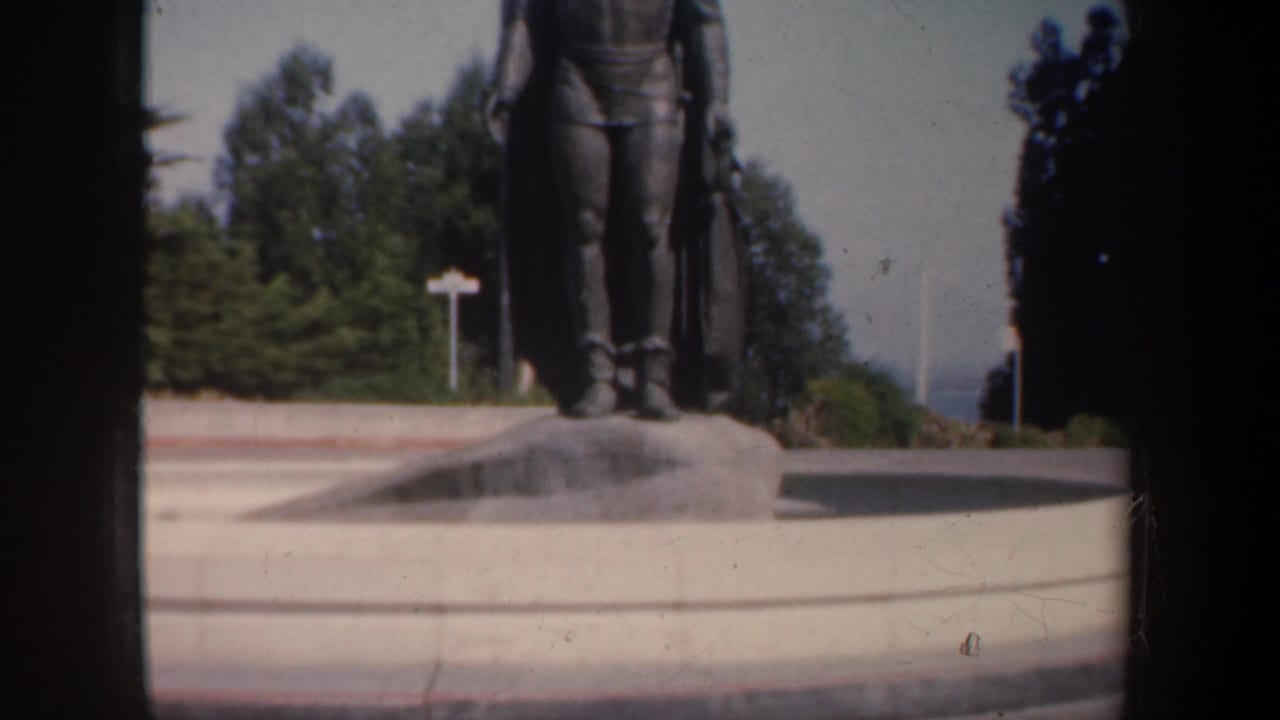 Lower portion of a statue on a pedestal with trees behind it.