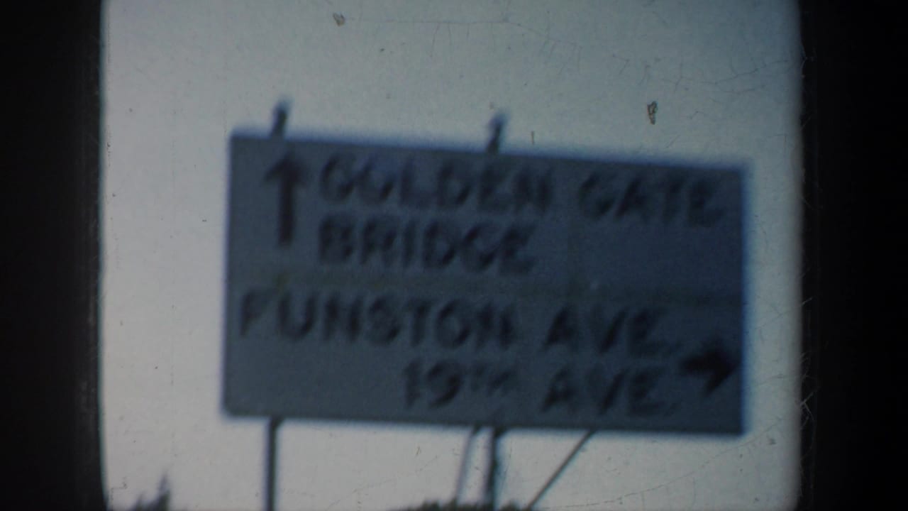 Road sign for Golden Gate Bridge and Funston Ave seen through a dark window frame.