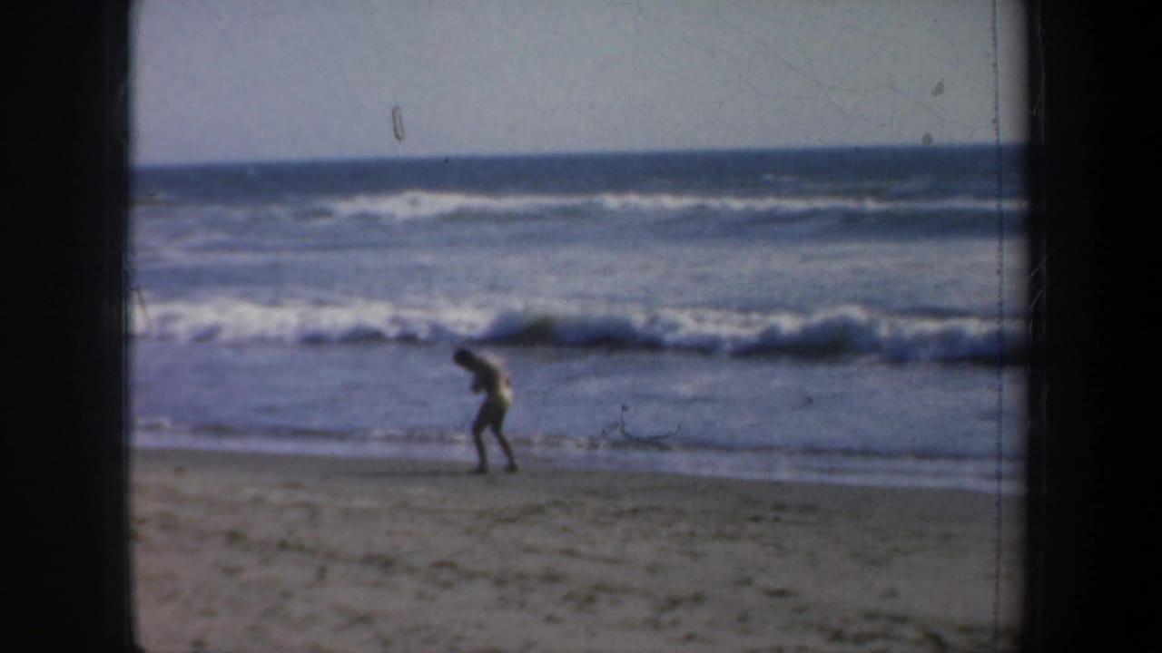 Man bends forward near the surf while practicing movements on the beach.
