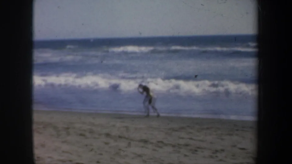 8mm home-movie frame from the supplied 1957 San Francisco beach clip showing the man moving along the sand during boxing practice.