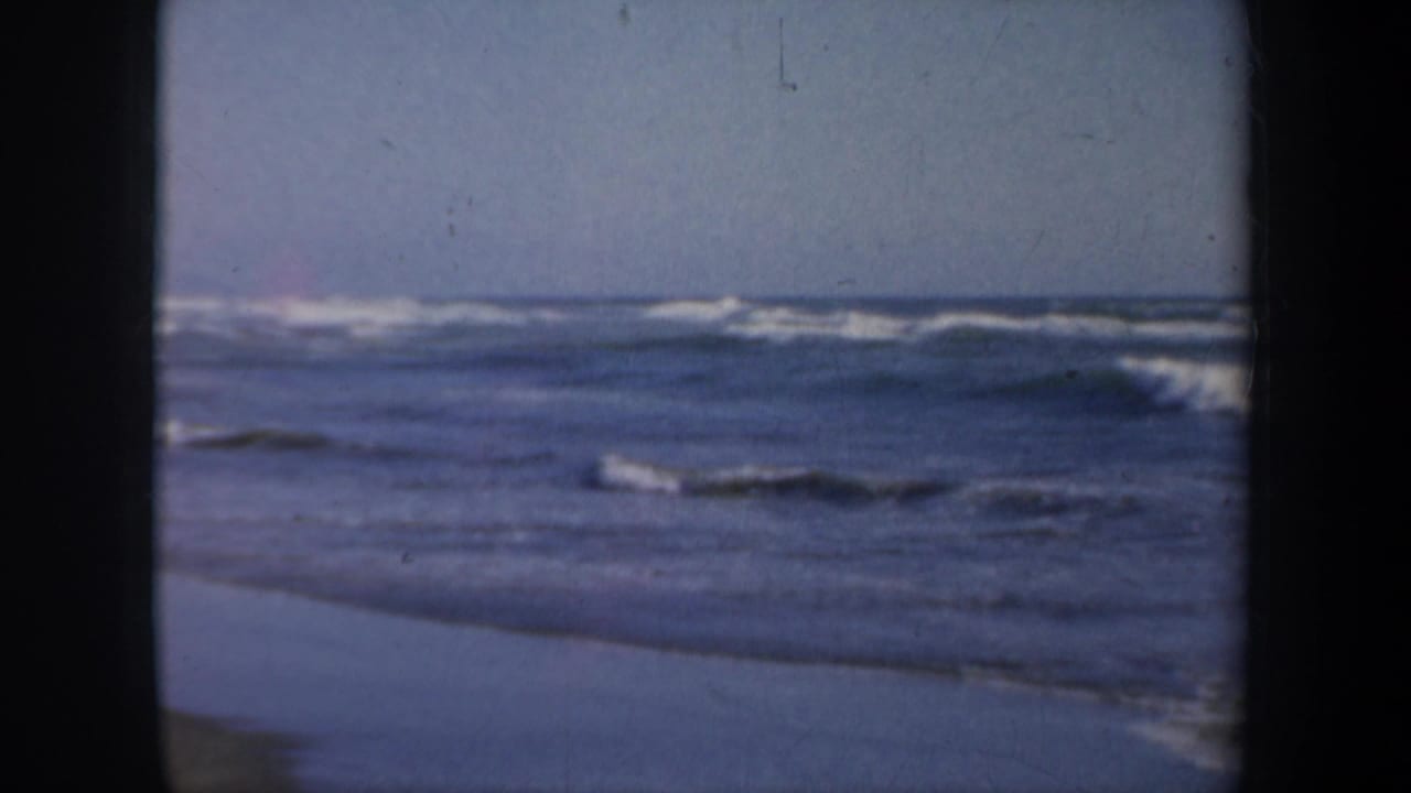 1957 San Francisco coastal home-movie frame showing waves, wet sand, and a broad ocean view.
