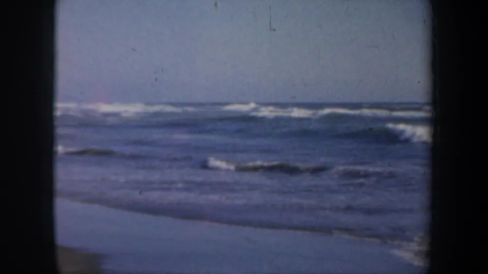 1957 San Francisco coastal home-movie frame showing waves, wet sand, and a broad ocean view.