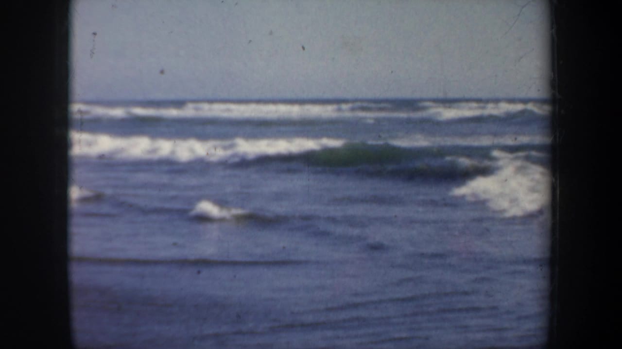 1957 San Francisco 8mm frame showing ocean surf and white foam under a pale sky, with visible film gate edges.