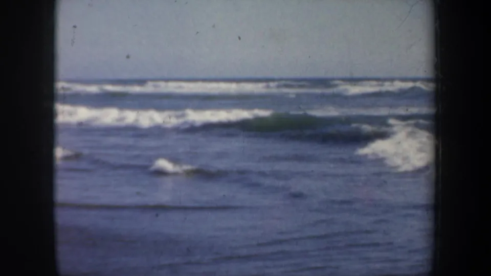 1957 San Francisco 8mm frame showing ocean surf and white foam under a pale sky, with visible film gate edges.