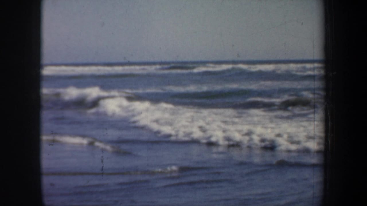 Breaking surf and low horizon framed by dark film edges.