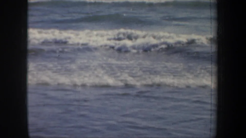 1957 San Francisco 8mm frame focused on surf washing toward wet sand, with soft focus and visible film texture.