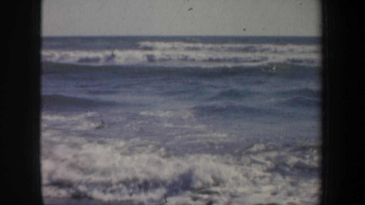 Ocean horizon and rolling surf fill the frame, with dark vertical film borders on both sides.