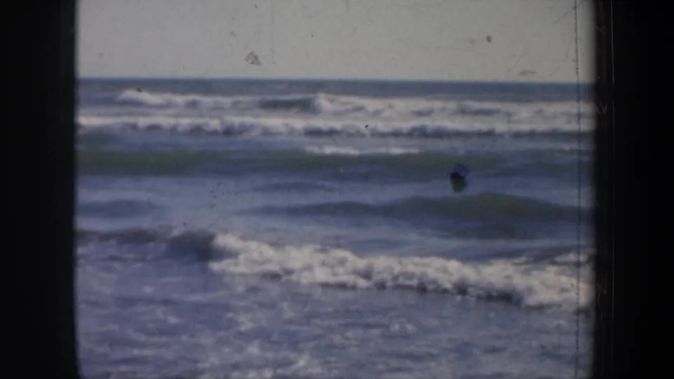 Vintage 8mm San Francisco surf frame from 1957 showing cresting waves, white foam, and a small dark speck near the waterline.