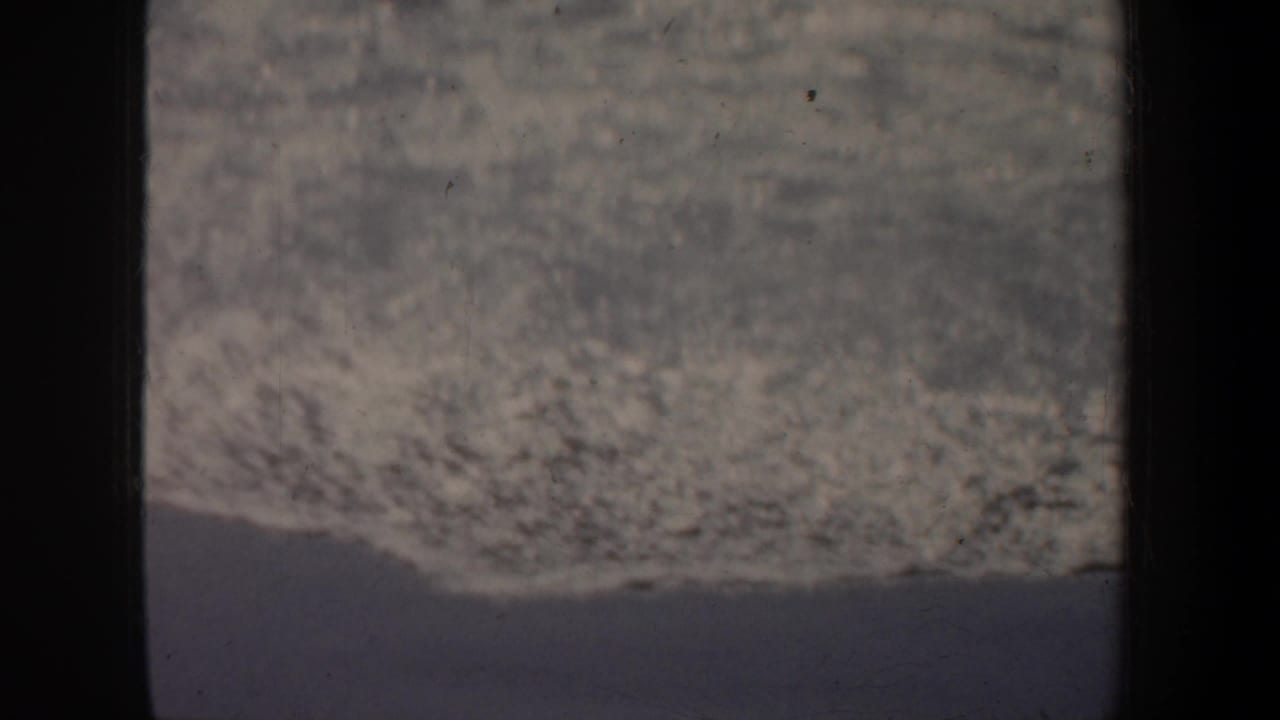 Grainy 1957 home-movie frame from San Francisco showing surf or shoreline with dark gate edges and a central divider.
