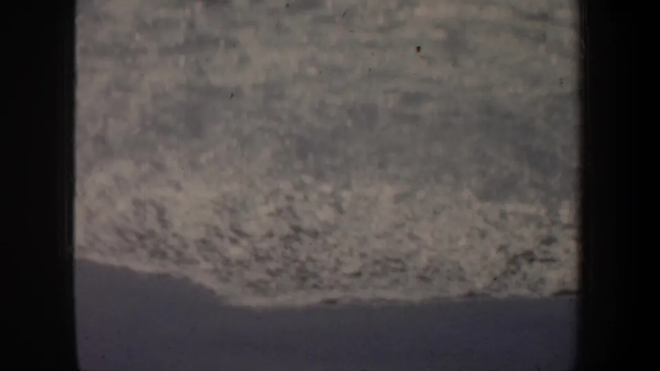 Grainy 1957 home-movie frame from San Francisco showing surf or shoreline with dark gate edges and a central divider.