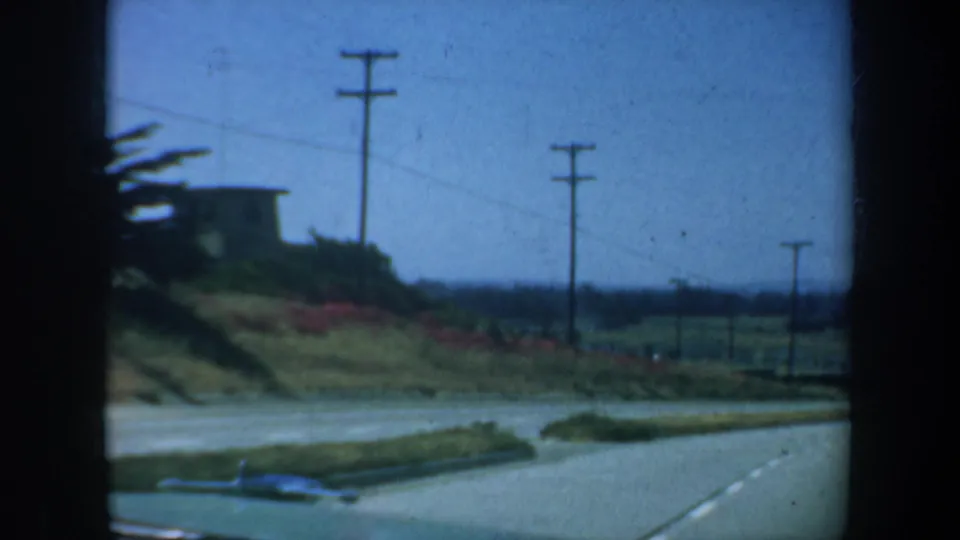 Brief 1957 San Francisco home-movie view of a road, utility poles, grassy verge, and a blue car near the edge of the clip.