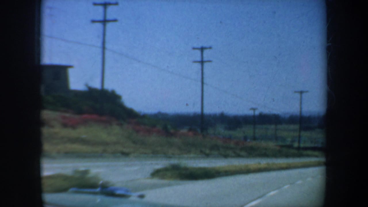 1957 San Francisco-area road view from a moving car, showing utility poles, a grassy embankment, and blue sky.