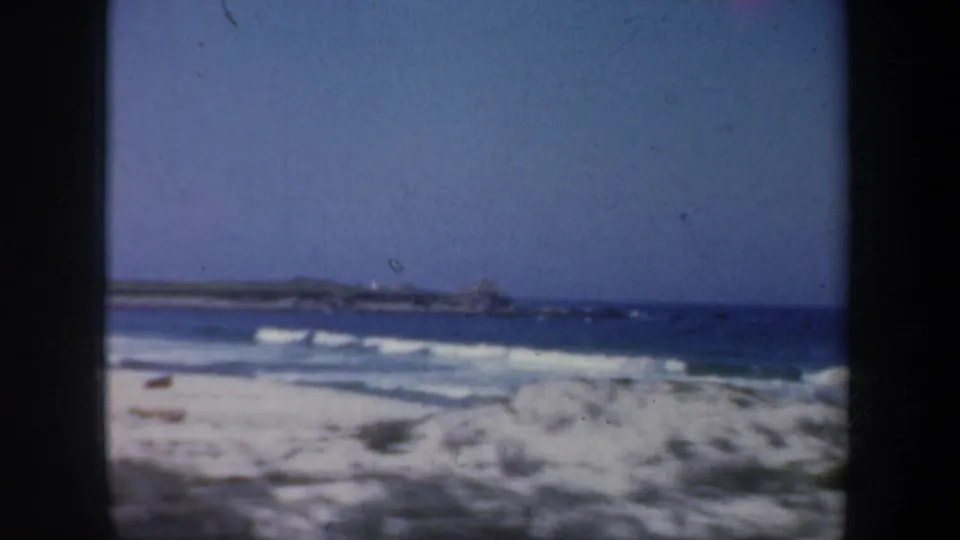 1957 San Francisco shoreline view with white surf, pale sand, blue water, and distant rocky coast.