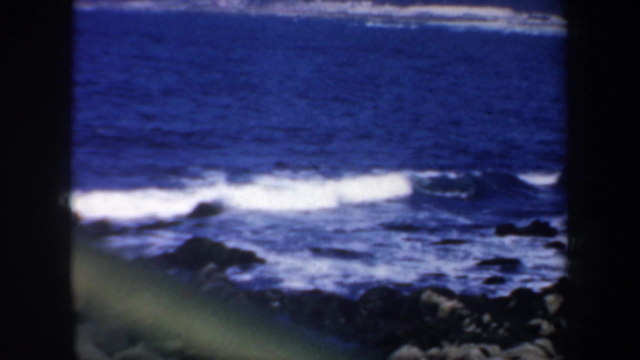 Vintage 8mm coastal view of white waves breaking across rocky surf in San Francisco, with a dark vertical film edge visible.