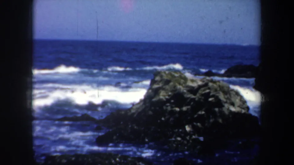 1957 San Francisco 8mm view of a large dark coastal rock with white surf and open ocean beyond.