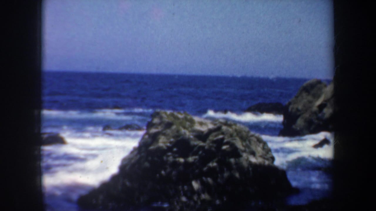 Rocky ocean shoreline with waves breaking under a blue sky.