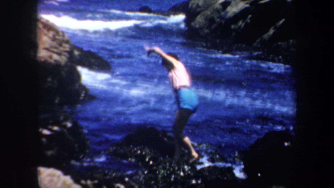 Adult swimmer leans across dark rocks near foamy water.