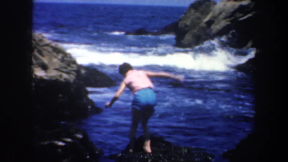 Adult swimmer on a rugged San Francisco shoreline bends near blue water and white breaking waves.