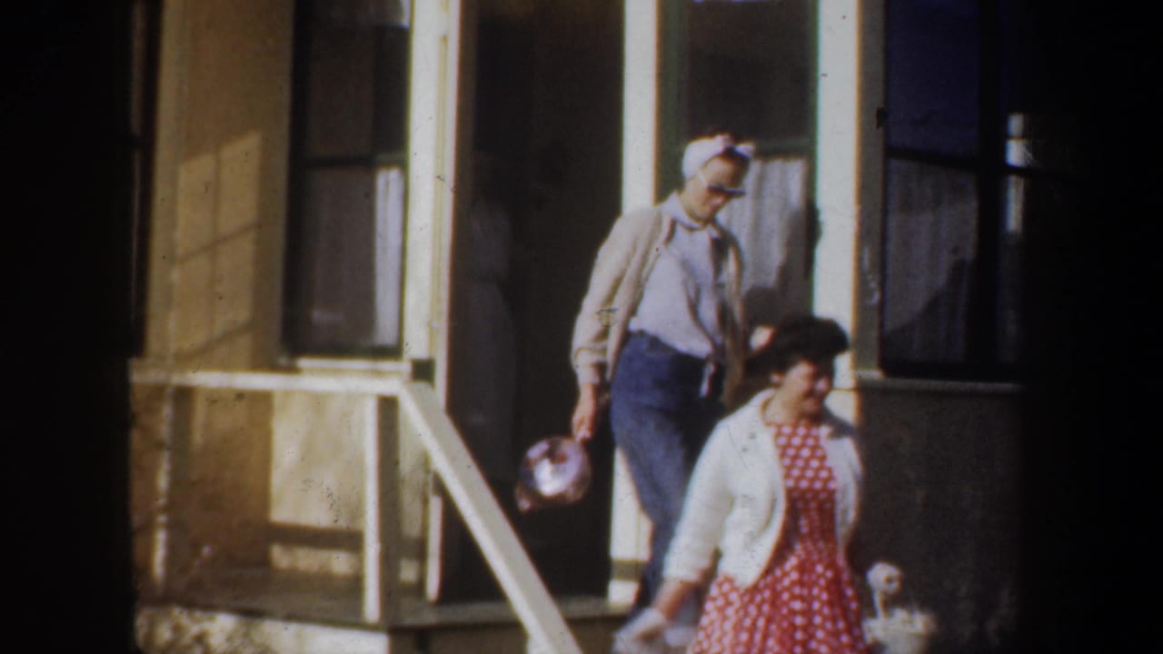 In supplied 1957 Portland home-movie footage, two adult women leave a porch while a doorway and curtained windows frame the scene.
