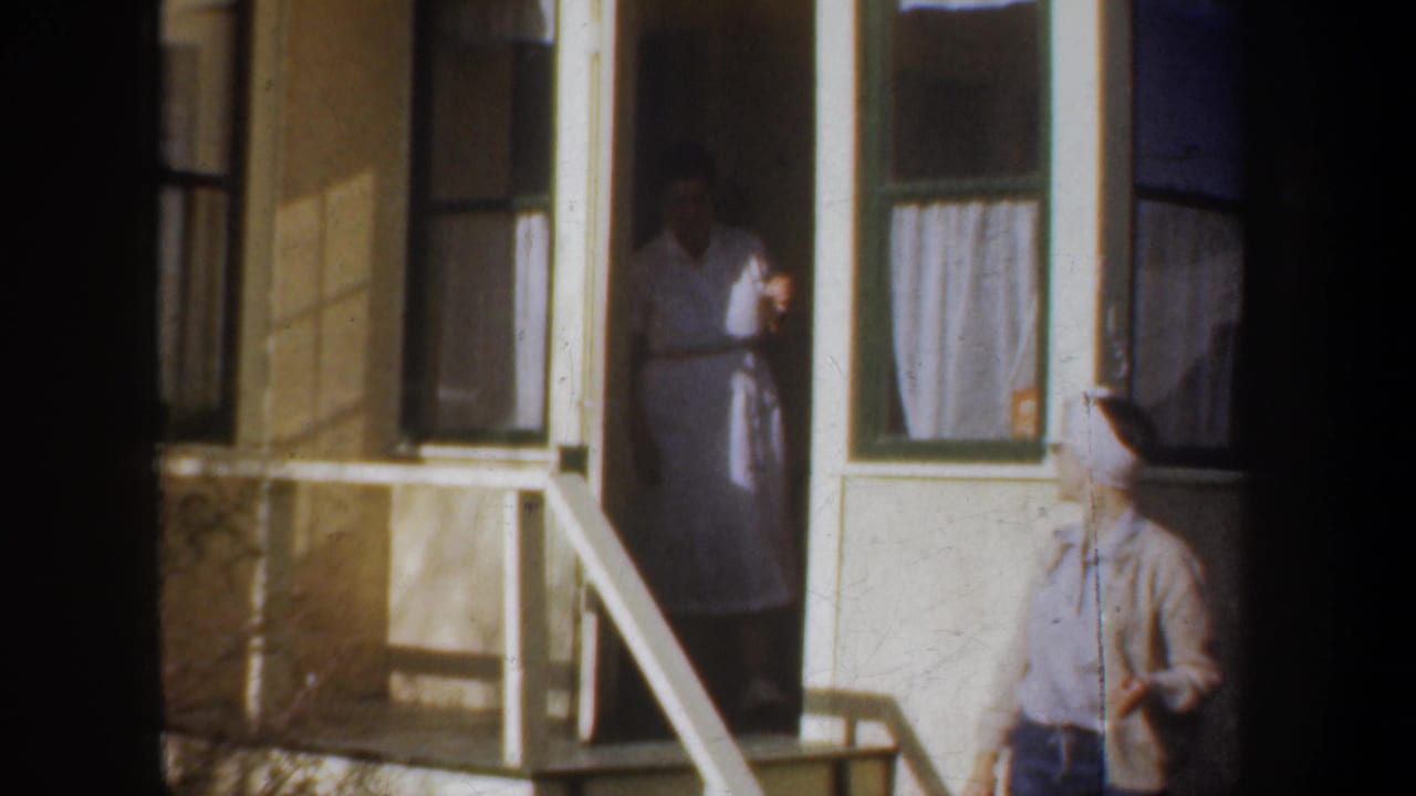 A woman stands in a doorway while another woman in a headscarf is near the porch steps.