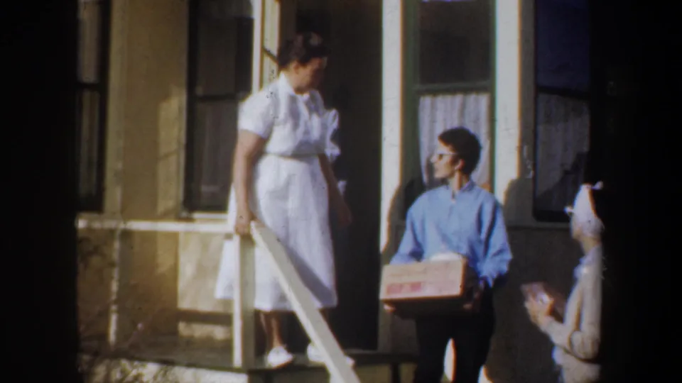The final frame shows two adult women on the porch, one standing in a white dress and one seated with a cardboard box, in 1950s home-movie color.