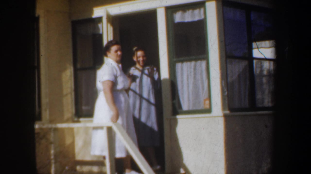 Two women on a Portland porch in 1957 appear to pause during a friendly goodbye, with house windows and a white railing behind them.