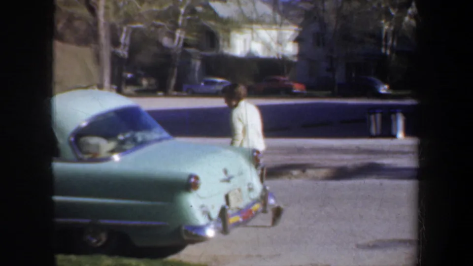 The traveler continues past a pale green 1950s car on a quiet Portland street, with houses and parked cars in the background.