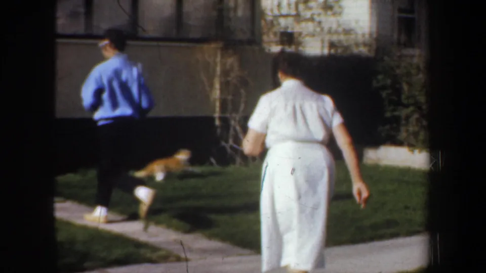 1957 Portland yard scene with a man in a blue sweater, a woman in white, and a cat visible on the lawn.