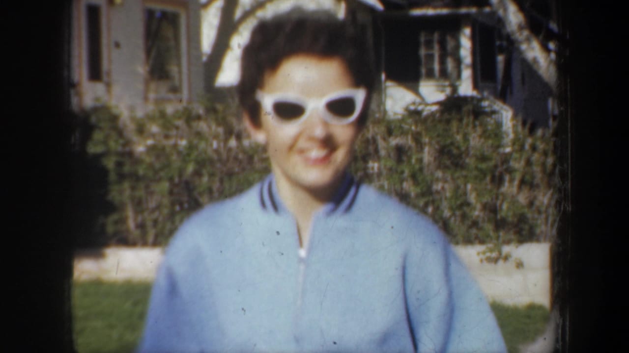 Close view of woman in blue sweater and white sunglasses smiling outdoors.