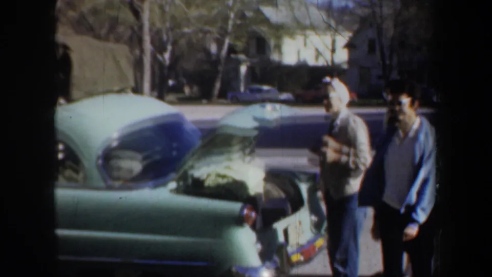 Young adults stand by a light green classic car with its hood raised in the supplied Portland 1957 home-movie clip.