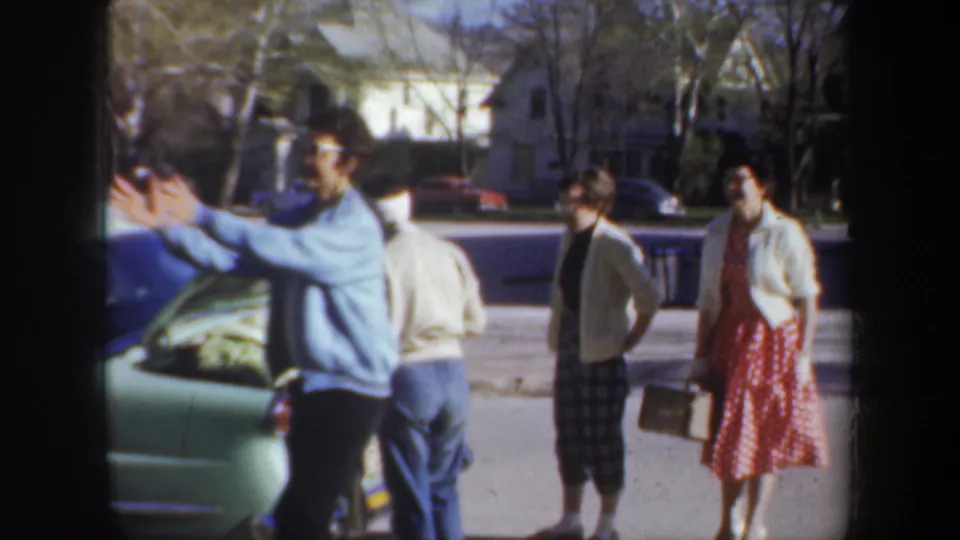 A man reaches toward the open car while others in 1950s clothing stand nearby on a Portland residential street.