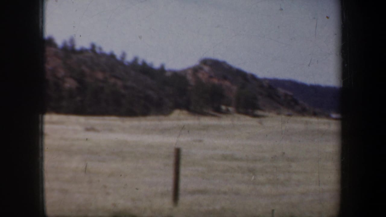 Rocky hill and open grassland framed by dark window edges.