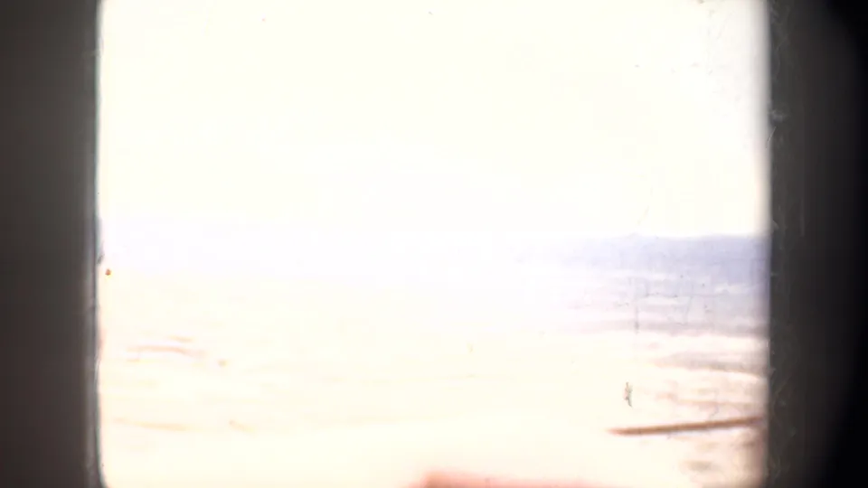 Overexposed final 1957 8mm frame with a dark window edge, faint landscape horizon, and washed-out sky from the moving vehicle view.