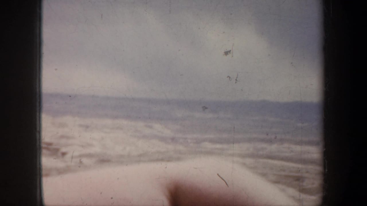 Blurred open landscape seen through film gate edges under a cloudy sky.