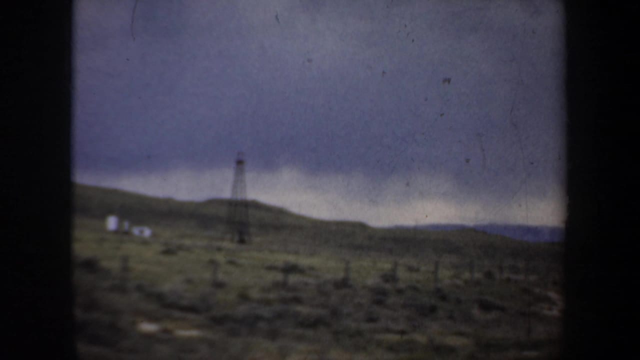 Distant utility tower and small structures on open ground beneath dark clouds.