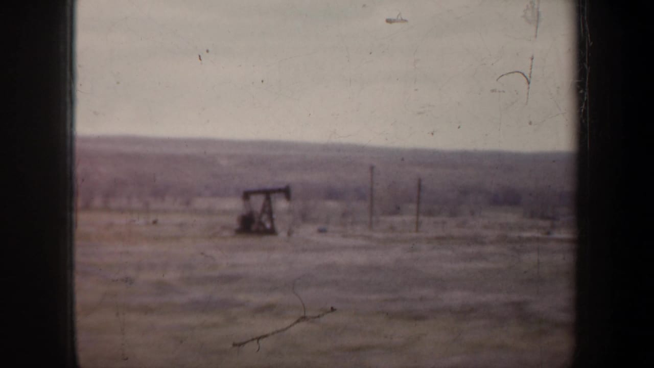 Oil pump jack in a flat open field seen through dark window edges.
